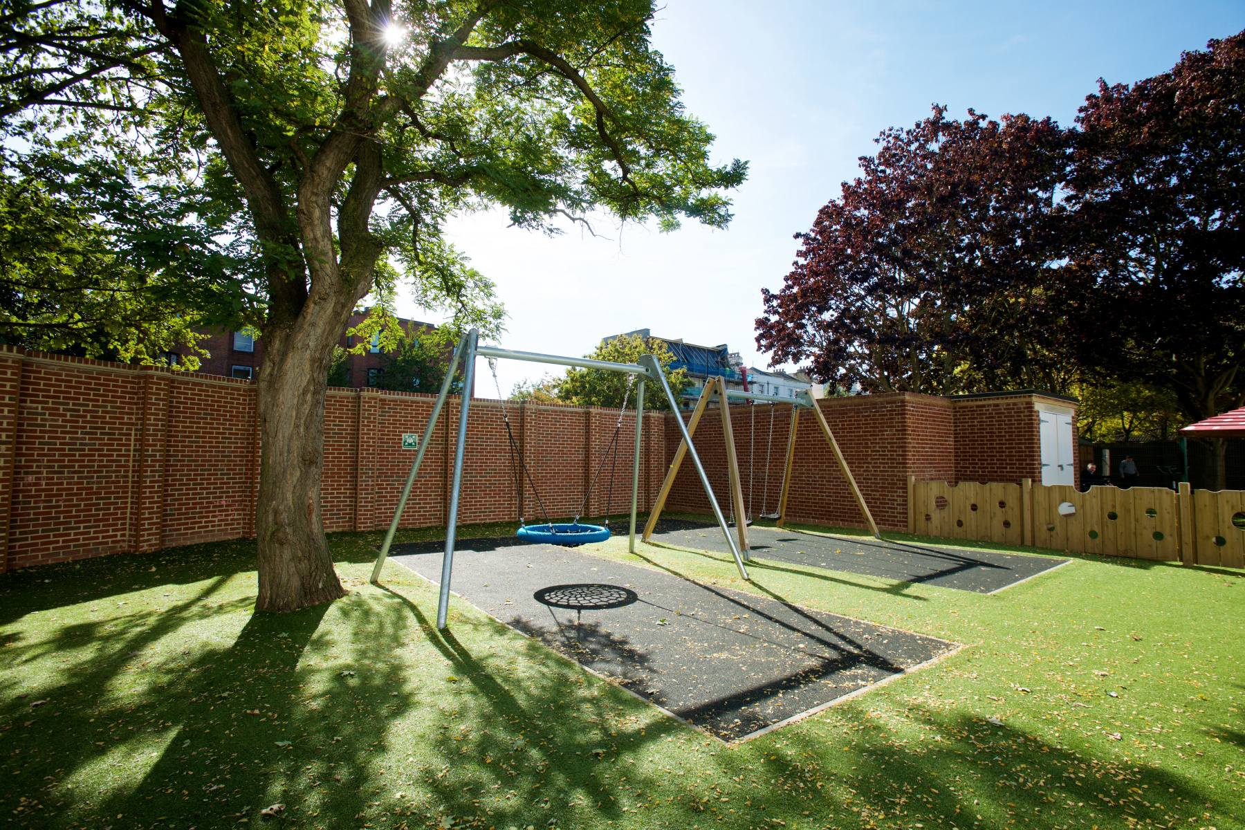 Large modern swing in a walled garden with a large tree in the sunshine